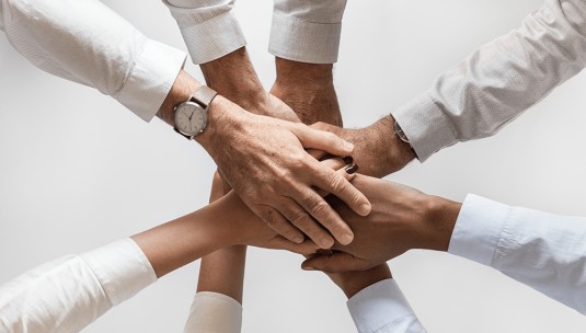 A group of employees with their hands in a circle showing teamwork.